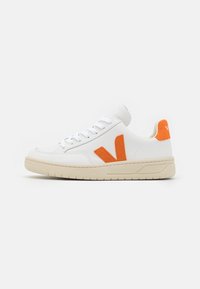 Baskets en cuir blanc avec des accents en suede orange, présentant un bout arrondi, des lacets plats et une semelle en caoutchouc beige. Design simple et texture lisse.