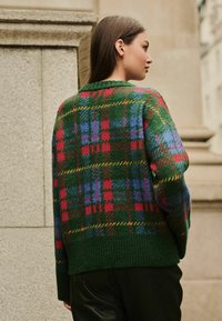Pletený sveter s zeleným základom a károvaným vzorom v červenej, modrej a žltej farbe, s rebrovaným lemom a voľným strihom.