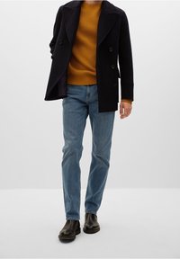 Navy double-breasted coat over a mustard ribbed sweater, paired with light blue jeans and black ankle boots. Minimalist design and fitted shape.
