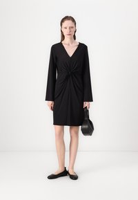 Must mustaga, V-kaelakaelusega, pikkade varrukatega ja keeratud esiküljega disain, valmistatud siledast kangast. Kantud lame mustade kingade ja väikese käekotiga.