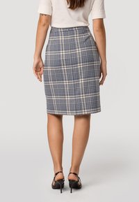 Jupe à carreaux bleu marine et beige, de longueur genou, avec une texture lisse, présentant un design ajusté et une taille discrète. Chaussures à talons hauts noires.