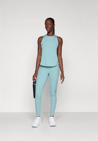 Un débardeur de sport bleu aqua et un legging, faits d'un matériau extensible, associés à des baskets blanches. Le legging présente un détail de logo subtil.