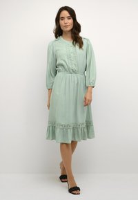 Mint green dress with balloon sleeves, embroidered detailing, and a gathered waist. ruffled hem accentuates the flowy fabric texture.