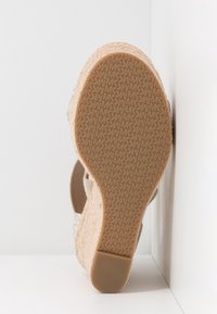 Semelle d'une sandale compensée avec une semelle en caoutchouc texturé ornée d'un motif de logos "MK", talon plateforme tissé beige clair.