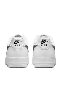 Baskets en cuir blanc avec un accent gris au niveau du talon, arborant un logo Nike Air noir à l'arrière et une semelle en caoutchouc texturé.