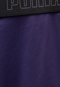 Κοντινό πλάνο σκούρου μοβ υφάσματος με μαύρη ελαστική ζώνη μέσης που φέρει τη λέξη "Polo" με γκρι ραφή.