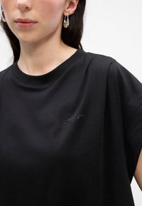 Černé bavlněné tričko s kulatým výstřihem, krátkými rukávy a subtlním vzorem rhinestones na hrudi, s jednoduchým designem podpisu.