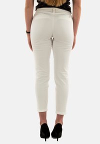 Pantalones blancos ajustados con cintura media, dobladillos con vuelta y dos bolsillos traseros, combinados con zapatos de tacón negro.