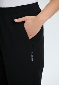 Zwarte elastische taillebandbroek met een zijzak. De stof is soepel met een subtiele glans, en voorzien van een klein logo in het wit gedrukt.