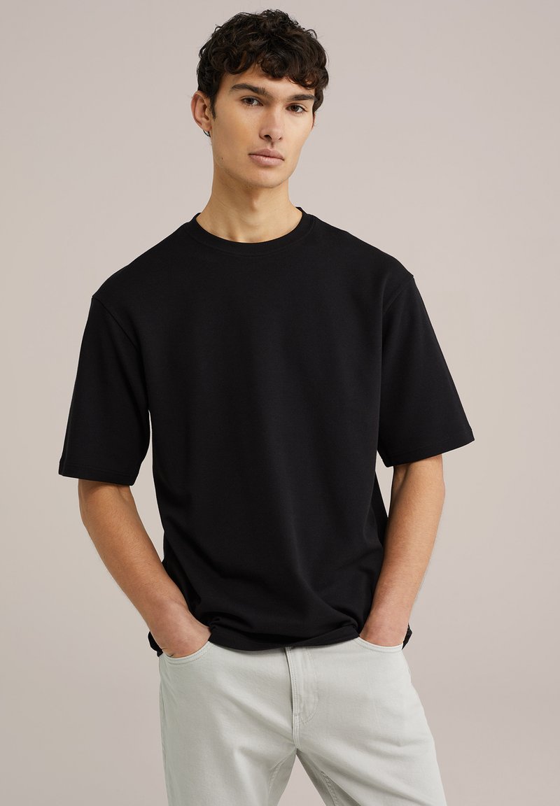 Černé bavlněné tričko s krátkými rukávy, kulatým výstřihem a volným střihem, doplněné o světlé kalhoty. Hladká textura; minimalistický design.