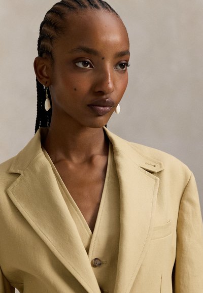 Σακάκι σε απαλό κίτρινο ύφασμα με δομημένο σχέδιο, γιακάδες με σχισμή και κλείσιμο με ένα κουμπί, σετ με αντίστοιχο γιλέκο και σκουλαρίκια.