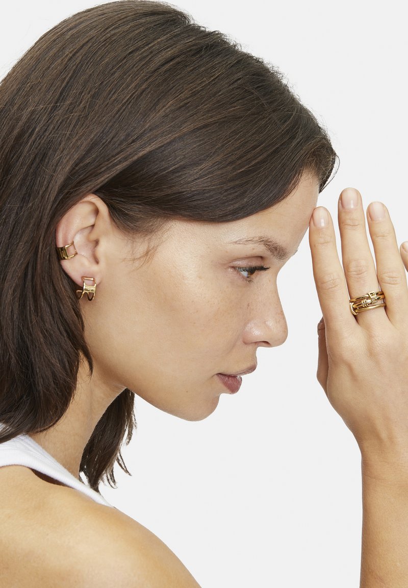 Schmuck in Goldoptik mit polierter Oberfläche, bestehend aus zwei Ohr-Cuffs und einem geschichteten Ring mit dekorativen Akzenten. Ausgefeilte Textur und modernes Design.