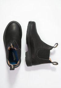 Botas de cuero negro hasta el tobillo con paneles laterales elásticos, punta redondeada y tira de agarre en el talón. Suela de goma plana, superficie texturizada para mayor agarre.