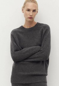 Pull en gris surdimensionné en tissu doux et texturé ; présente un col rond, des poignets et un ourlet côtelés pour une coupe décontractée.