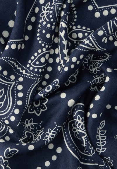 Υφάσμα σε ναυτικό μπλε με λευκά σχέδια παϊδάς και λουλουδιών, που περιλαμβάνει τελείες και περίπλοκα σχέδια, παρουσιάζοντας μια μαλακή, υφή επιφάνεια.