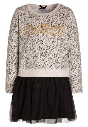 Beige langærmet kjole med sorte prikker, guld "sweet" tekst på brystet og tilhørende sort tylskørt.