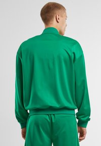 Sudadera verde con cuello alto, mangas largas y corte relajado. Fabricada en una tela suave y ligera, con puños y dobladillo acanalados.
