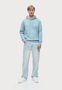 Ανοιχτό μπλε φούτερ με κορδόνια και εμπρόσθια τσέπη, σε συνδυασμό με ανοιχτό χρώμα τζιν παντελόνι και λευκά sneakers. Μαλακό, χαλαρό ύφασμα.