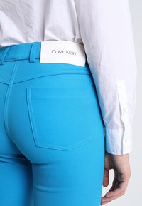 Jeans en denim bleu Calvin Klein avec une finition texturée, dotés d'une étiquette logo blanche à la taille et d'une poche arrière unique.