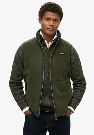 Green fleece vest with a full zipper and high collar, worn over a textured gray sweater. Features blue trim and a logo on chest pocket.