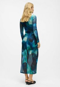 Robe à manches longues en tissu transparent ornée d'un motif aquarelle abstrait bleu-vert, silhouette ajustée et design long jusqu'au sol.