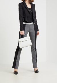 Zwarte peplumblazer over een grijs-zwart geruit patroonbroek. Witte handtas met een gestructureerde vorm en zwarte puntige hakken.