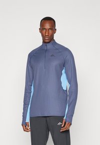 Haut zippé à manches longues bleu marine avec des accents bleu clair et un tissu texturé. Comprend un col haut et un design ajusté pour les vêtements de sport.