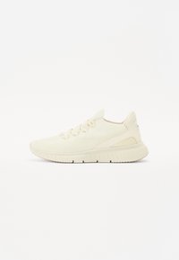 Light cream athletic shoe with a knitted mesh upper, lace-up design, cushioned midsole, and textured rubber outsole.