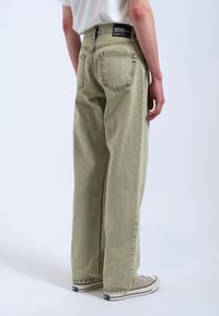 Ljusgröna denimjeans med rak skärning, bakfickor och en etikett på midjebandet. Har synlig sömnad och en lätt textur.