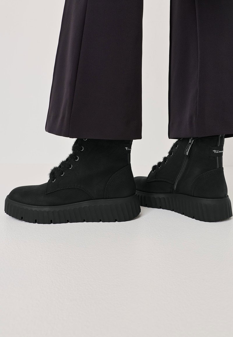 Schwarze Knöchelstiefel aus strukturiertem Leder, mit einer robusten Gummisohle, Schnürung auf der Vorderseite, Reißverschluss und Fell-Akzenten.