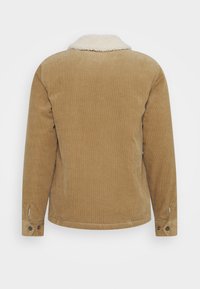 Brązowa kurtka z korduroy z miękkim kołnierzem z owczej wełny, długimi rękawami i guzikami na mankietach. Strukturalny materiał o luźnym kroju.