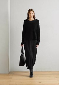 Suéter negro de canalé combinado con una larga falda negra y botas negras con cordones. Lleva un bolso tote negro. Look sencillo y monocromático.
