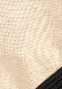 Tissu tricoté beige avec un petit trou près du centre et un bord noir visible dans le coin inférieur droit.