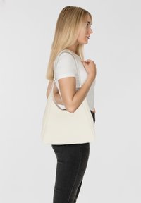 Bolso de hombro de cuero sintético blanco con forma triangular, textura suave y correa ajustable, expuesto sobre un fondo neutro.