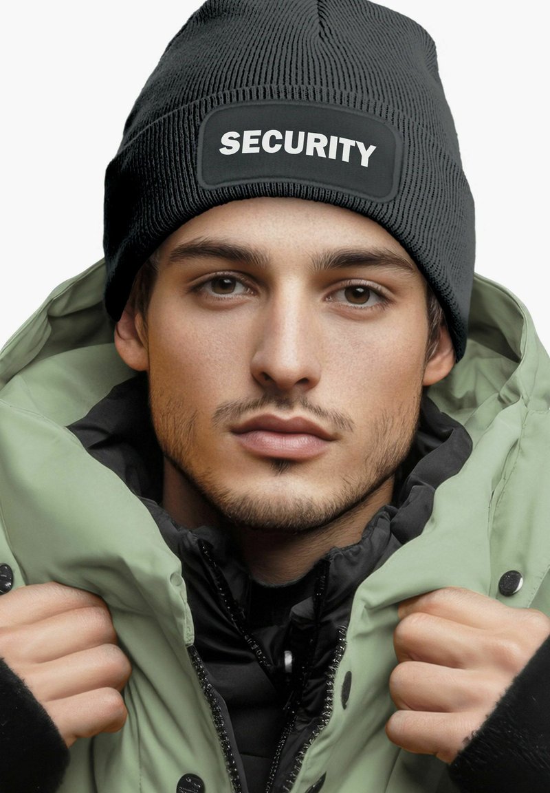 Schwarze gerippte Mütze mit "SECURITY" Patch. Grüne Steppjacke mit schwarzem Innenfutter, hoher Kragen und Knopfverschluss.