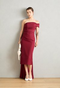 Rochie de seară burgundy, fără bretele, cu o siluetă ajustată și detalii de adunare pe lateral. Asortată cu pantofi albaștri cu bot ascuțit și o geantă mică albă.