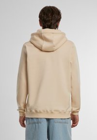 Beige pullover hoodie lavet af blødt stof, med en stor hætte, ribbede manchetter og en afslappet pasform. Glat tekstur med et enkelt design.