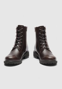 Paar dunkelbraune Leder-Schnürstiefel mit seitlichen Reißverschlüssen und klobigen schwarzen Sohlen auf einfachem hellem Hintergrund.