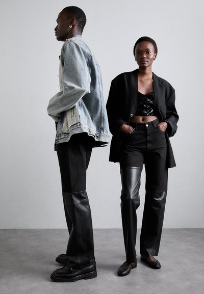 Denim jacket, black sequined crop top, oversized black blazer, black jeans with leather accents, and black shoes. Neutral background.