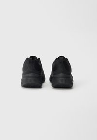 Baskets de sport noires avec un dessus en mesh texturé, un col rembourré et une semelle en caoutchouc flexible avec motif. Équipées de languettes pour un enfilage facile.