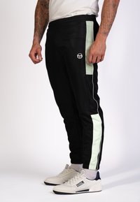 Schwarze Sporthose mit mintgrünen seitlichen Akzenten, slim fit, elastischem Bund und geripptem Saum. Logo auf der Vorderseite.