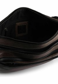 Interno di borsa in pelle marrone con molteplici scomparti con zip. Texture liscia e forma allungata, con fodera nera e patch del marchio.