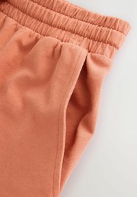 Tejido de color durazno con una textura suave que presenta una cintura elástica y detalles en las costuras laterales. Imagen de primer plano que destaca la calidad del material.