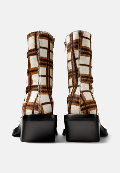 Faux fur anklar med ett brunt och vitt rutmönster, klack med blockhöjd och dragkedja bak. Den texturerade ytan ökar det visuella tilltalande.