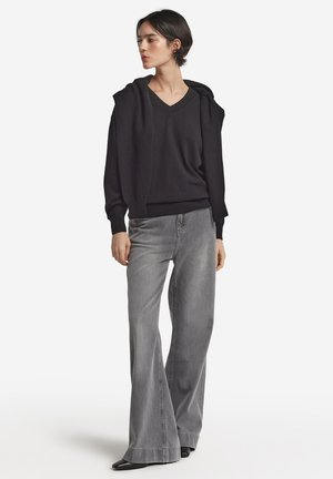Svart oversized hoodie med V-ringning och snörning, kombinerad med högmidjade grå utsvängda jeans. Slät textur, modern passform och rik färgkontrast.