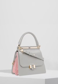 Borsa a tracolla in pelle grigia con pannelli laterali in suede rosa, hardware dorato, manico superiore e tracolla removibile su un piedistallo bianco.