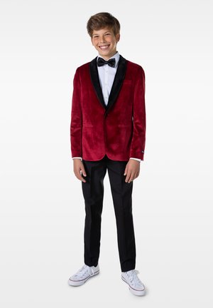 Blazer de terciopelo rojo con solapas de satén negro, camisa blanca, pajarita negra, pantalones negros y zapatillas blancas. Presenta un diseño de corte ajustado.