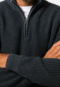 Pull over en tricot bleu foncé avec un zip mi-long, présentant un tissu texturé, des poignets côtelés et une coupe décontractée.