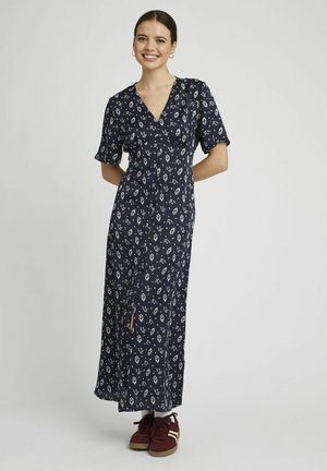 Robe maxi florale bleu marine avec un décolleté en V, des manches courtes et une fente sur le côté, associée à des baskets bordeaux et des chaussettes blanches.