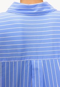 Lichtblauw coll shirt met horizontale en verticale witte strepen. Gemaakt van zachte stof met een geplooide achterkant.